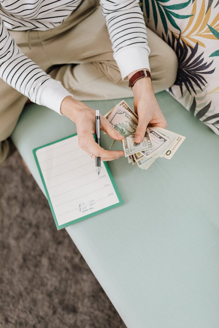 An individual counts money while sitting, holding a notebook and pen.
