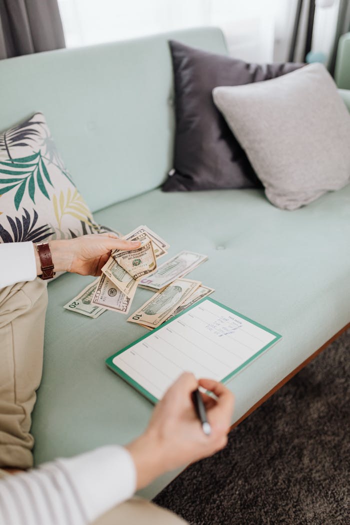 A person counting cash on a couch with a notebook, representing personal finance management.